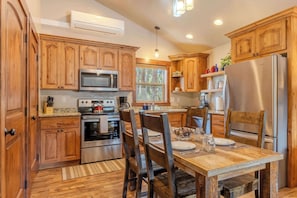 Una cocina con armarios de madera, electrodomésticos de acero inoxidable y un comedor con mesa y sillas de madera.