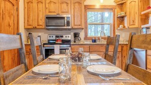 A wooden kitchen with a large island, built-in microwave, and a window overlooking a forest. - Burnt Hole (West Yellowstone)