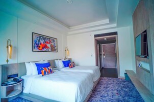 Habitación de hotel con dos camas, un televisor, un cuadro y una alfombra estampada.