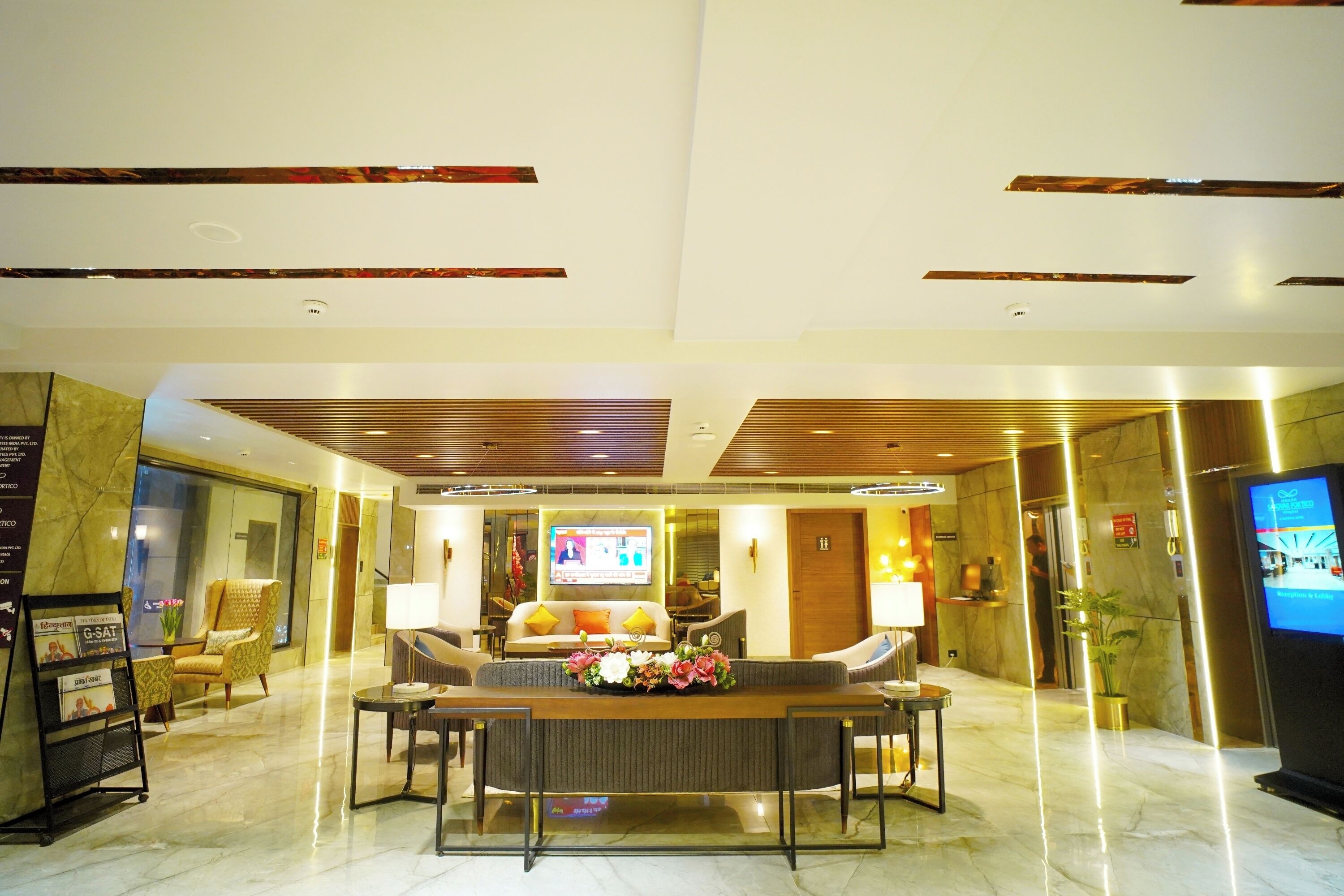 A modern lobby with a reception desk, seating area, and a television screen.