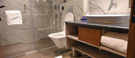 A modern bathroom with a glass shower enclosure, a white toilet, a marble-tiled wall, and a wooden vanity with a sink and towel storage.
