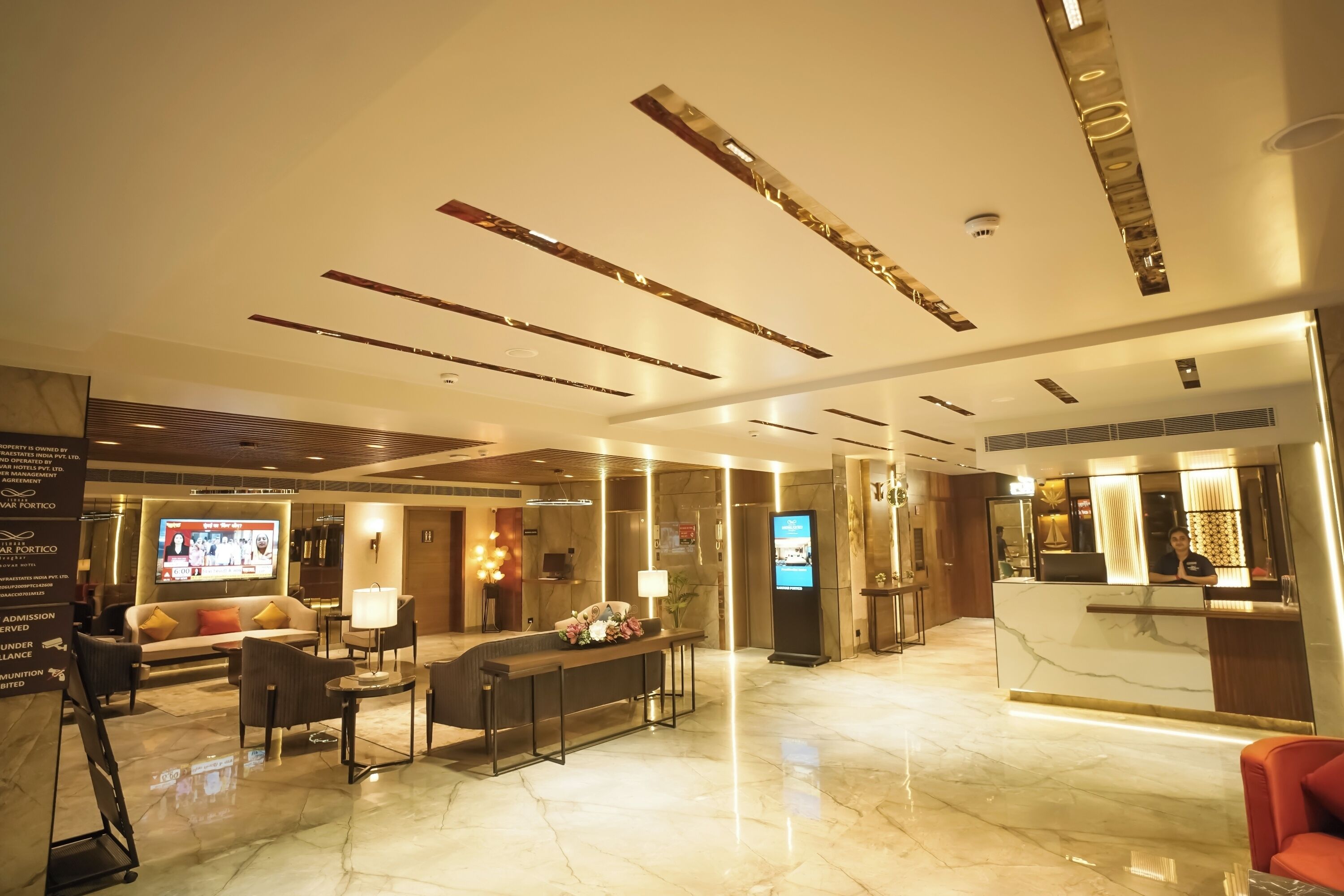 A modern hotel lobby with a reception desk, seating area, and a digital screen.