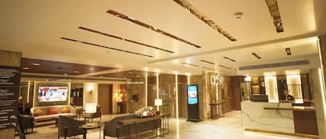 A modern hotel lobby with a reception desk, seating area, and a digital screen.