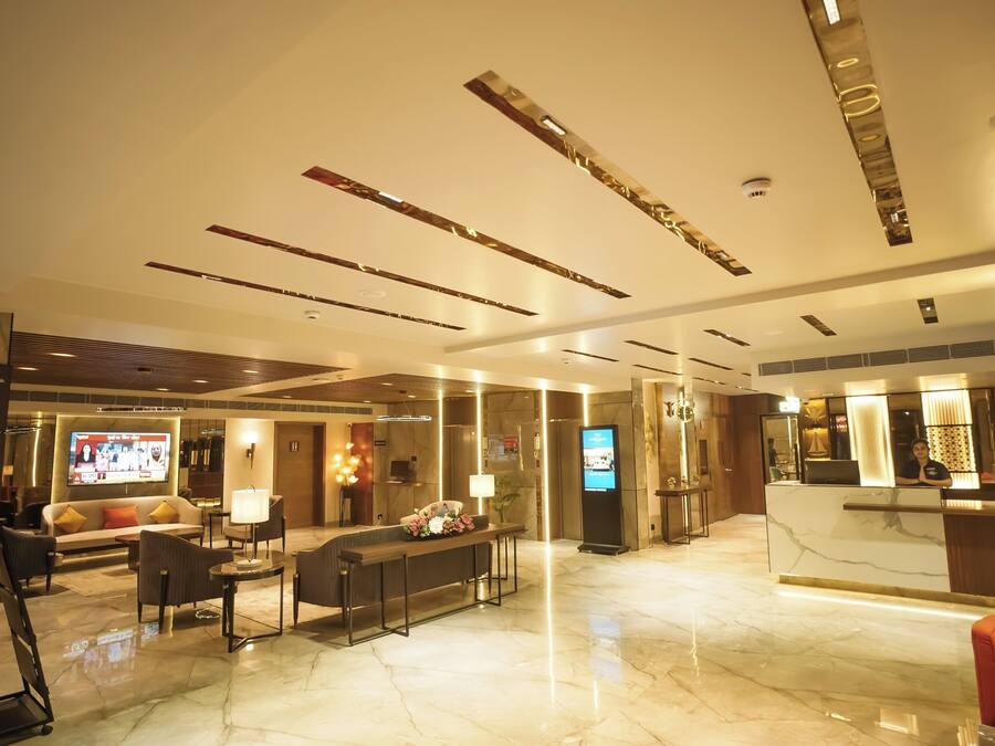 A modern hotel lobby with a reception desk, seating area, and a digital screen.
