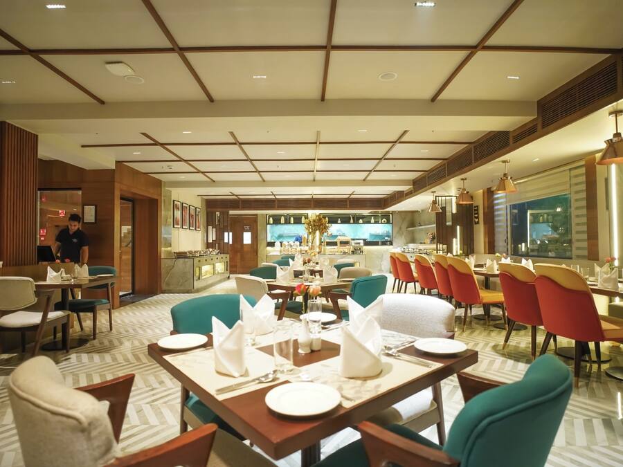 A restaurant with tables set for dining, a bar area, and a view of the kitchen.