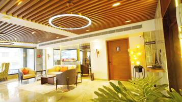 A modern lobby with wooden ceiling panels, a reception desk, comfortable seating, and a large plant.