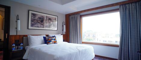 A hotel room with a large bed, a nightstand with a lamp, a framed picture on the wall, and a window with curtains.