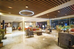 A modern hotel lobby with a reception desk, seating area, and a view of the cityscape through large windows. - Ishaan Sarovar Portico Deoghar (Deoghar)