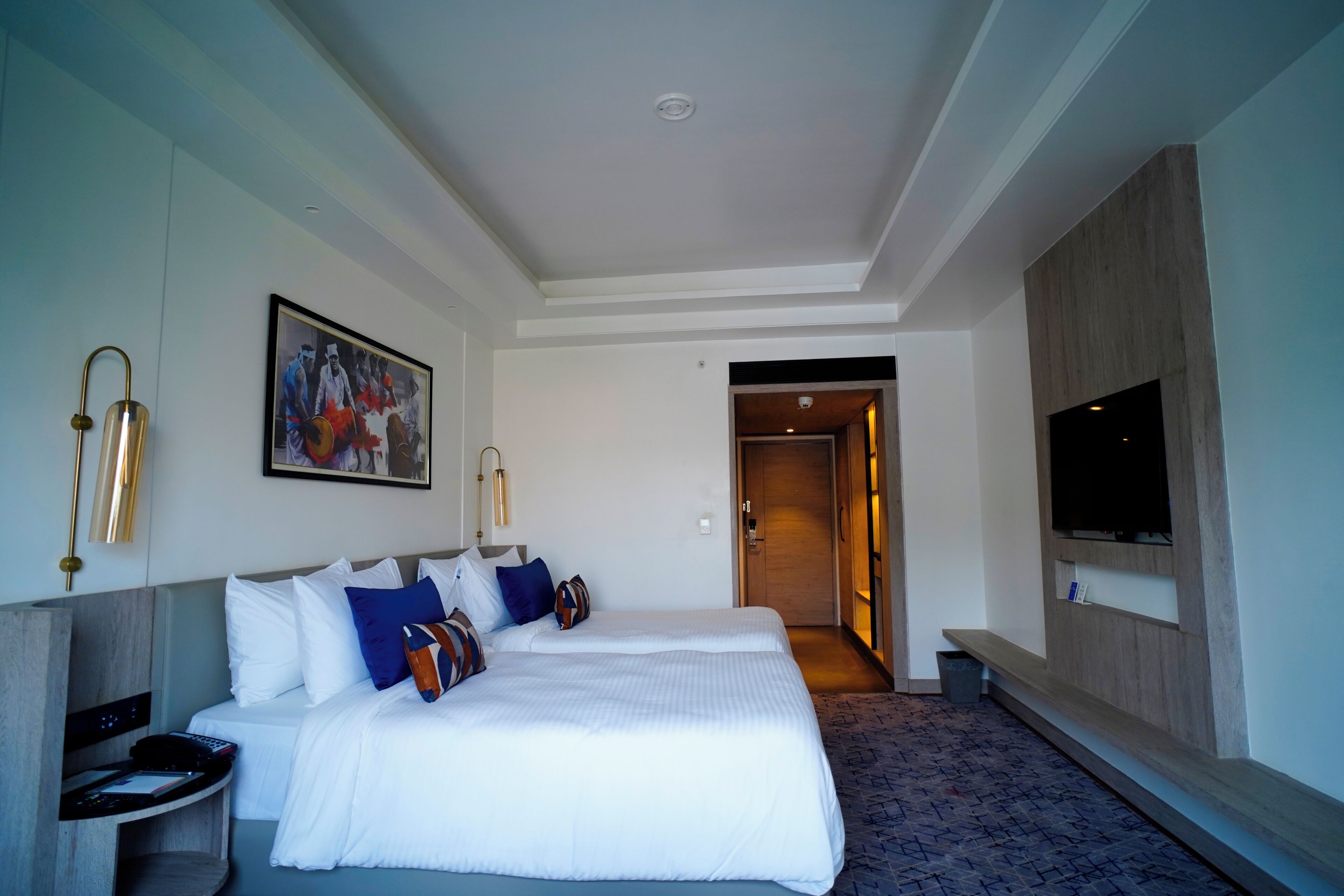 Ein Hotelzimmer mit zwei Betten, einem Fernseher, einem Gemälde und einem Schreibtisch mit Telefon.