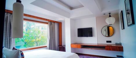 A hotel room with a large bed, a TV, a mirror, and a window with curtains.