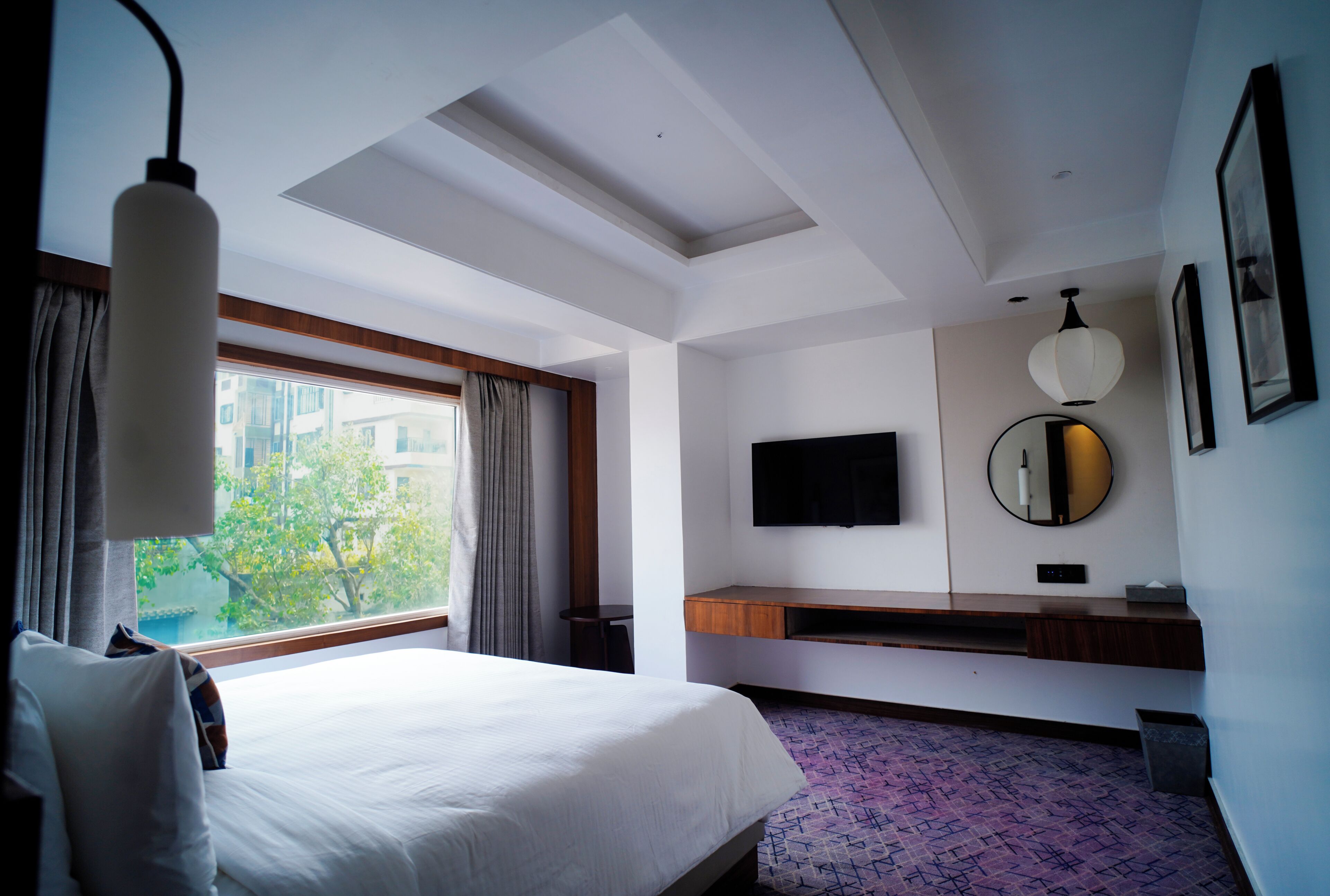 A hotel room with a bed, a TV, a mirror, and a window with curtains.