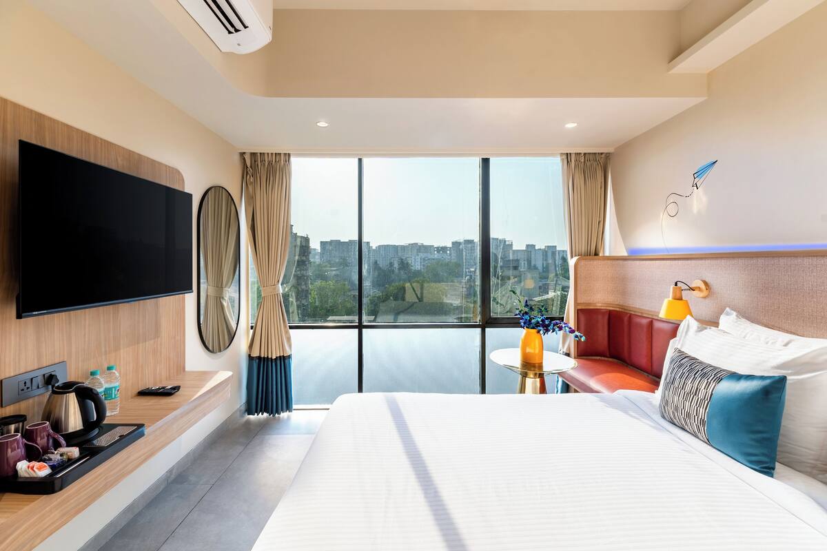 Ein modernes Hotelzimmer mit einem großen Bett, einem Flachbildfernseher, einer Sitzecke und Blick auf die Stadt.