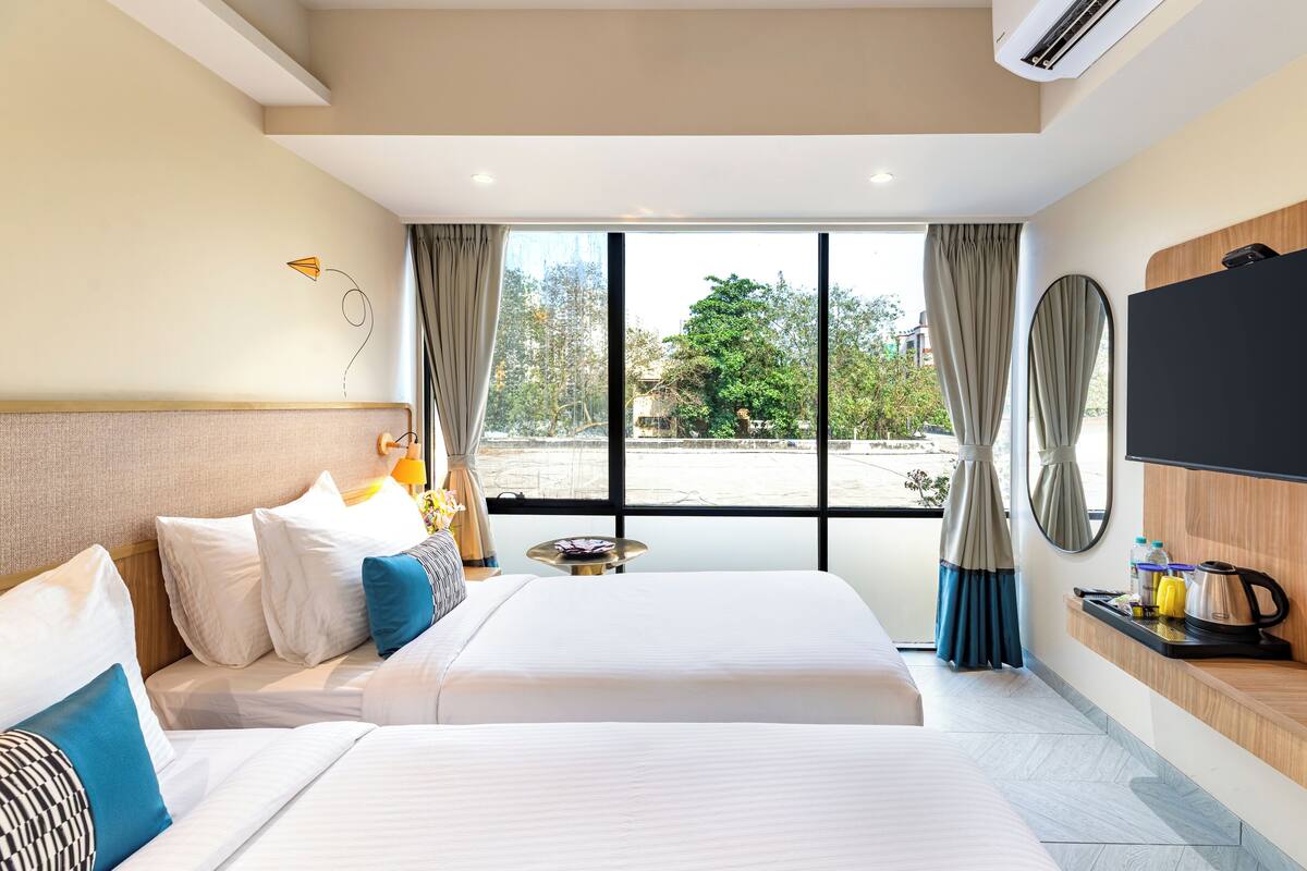 Ein Hotelzimmer mit zwei Betten, einem großen Fenster, einem Flachbildfernseher und einem kleinen Tisch mit Wasserkocher.