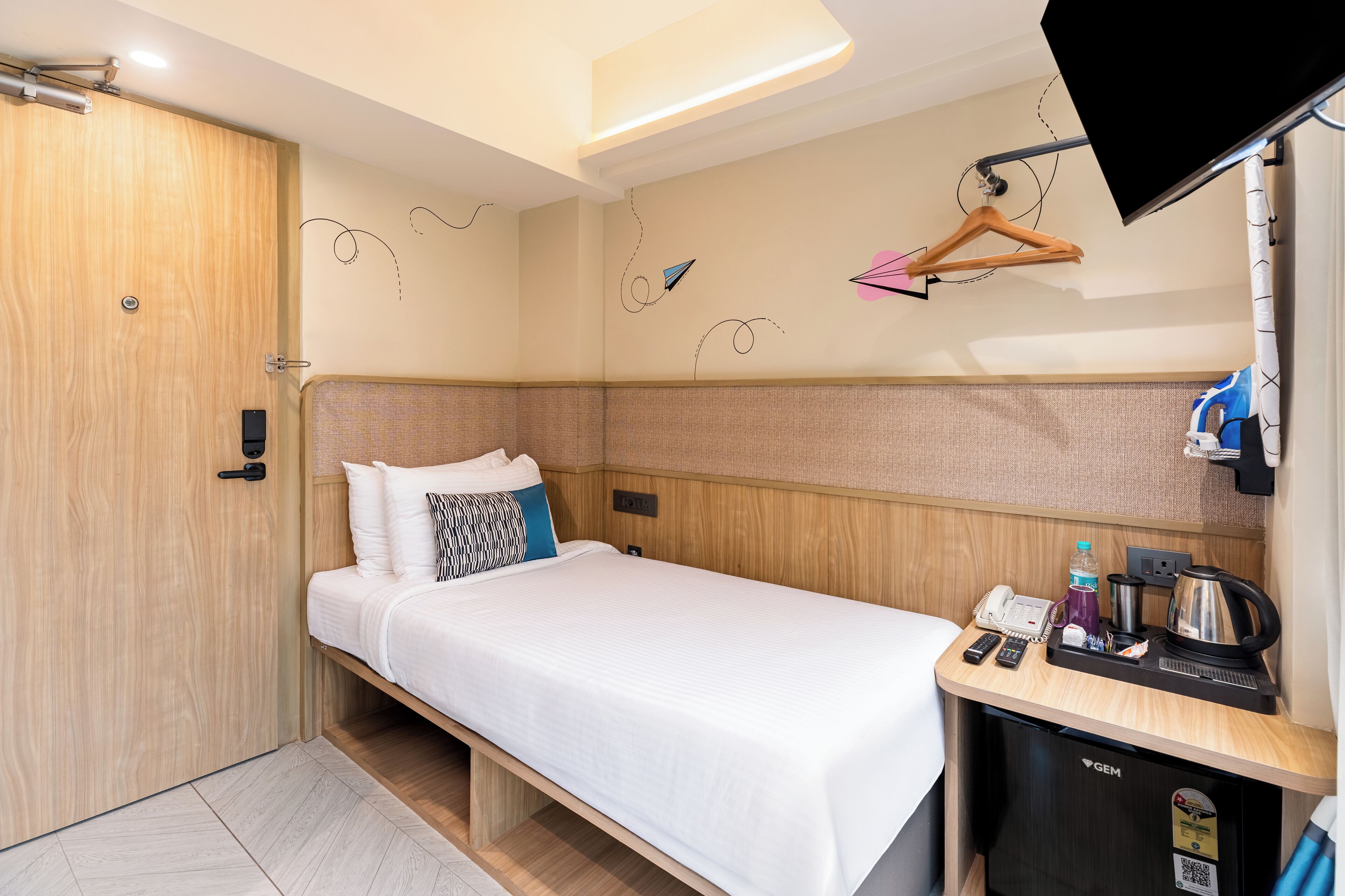 A compact hotel room with a single bed, a small desk with a phone, a kettle, and a coffee maker.