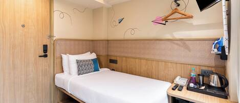 A compact hotel room with a single bed, a small desk with a phone, a kettle, and a coffee maker.
