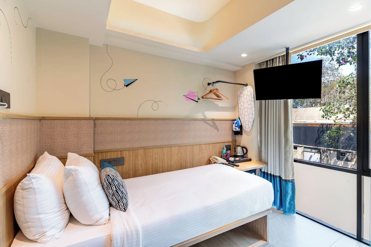 Ein modernes Hotelzimmer mit einem großen Bett, einem Nachttisch mit Telefon und Wasserkocher, einem an der Wand befestigten Fernseher und einem Fenster mit Blick nach außen.