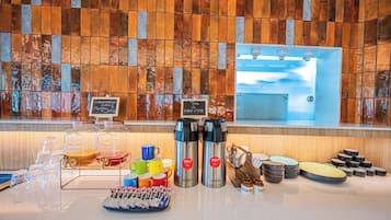 Un bufé de desayuno con diversas opciones de comida, una estación de café y vistas al mar a través de una ventana.