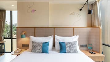 A hotel room with a large bed, two bedside tables, a nightstand, a lamp, a phone, and a view of the city through the window.