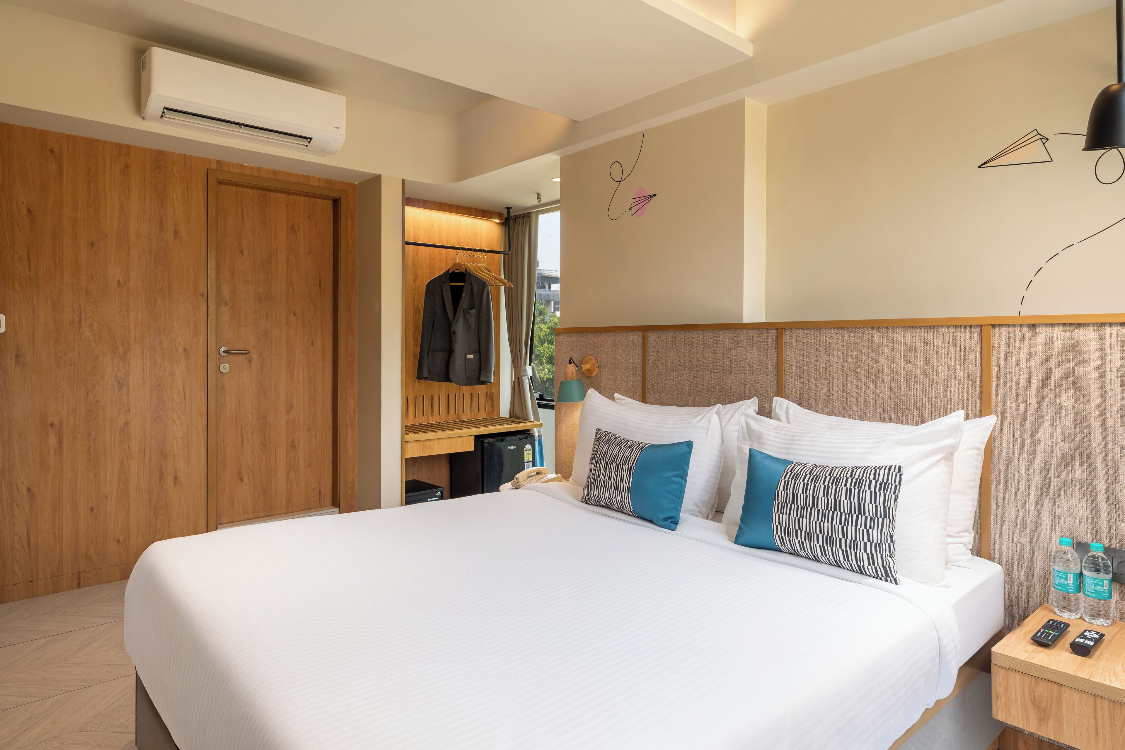 A hotel room with a large bed, a wooden wardrobe, a desk with a lamp, and a wall-mounted air conditioner.