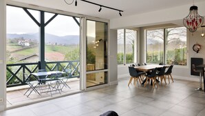 A spacious dining area with a large table and chairs, a balcony with a view of the countryside, and a modern chandelier. - Architect-designed house with swimming pool 10 minutes from St Jean de Luz (Urrugne)