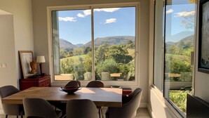 A dining area with a large window offering a view of a mountainous landscape. - Architect-designed house with swimming pool 10 minutes from St Jean de Luz (Urrugne)
