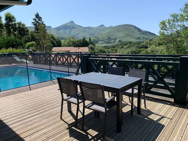A wooden deck with a pool and chairs overlooking a mountainous landscape.