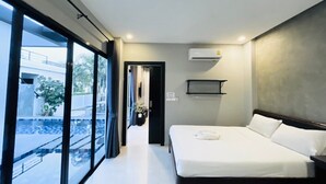 Une chambre d’hôtel moderne avec un grand lit, une petite table de chevet, un climatiseur fixé au mur et une vue sur une piscine et un immeuble, le tout visible à travers de grandes fenêtres.