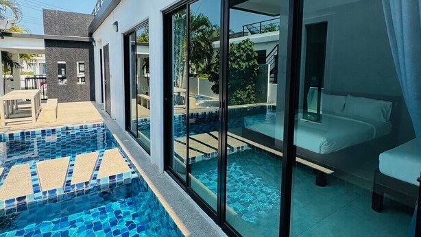Une chambre d’hôtel moderne dotée d’une grande porte vitrée donnant sur un balcon, un espace piscine privé et une vue sur le paysage environnant.