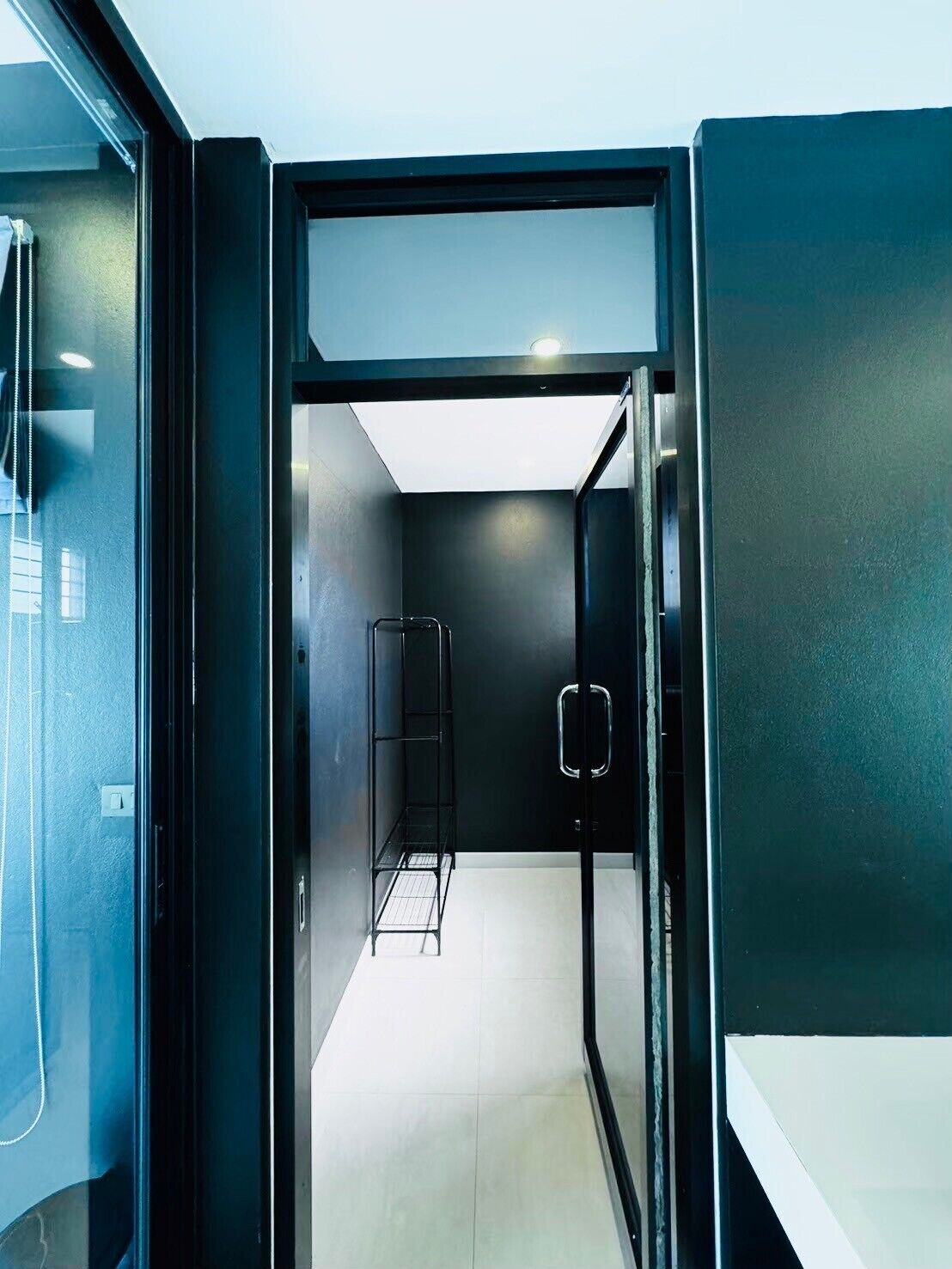 Ein modernes, minimalistisches Badezimmer mit Glasdusche, einem Metallregal und einer weißen Ablagefläche.
