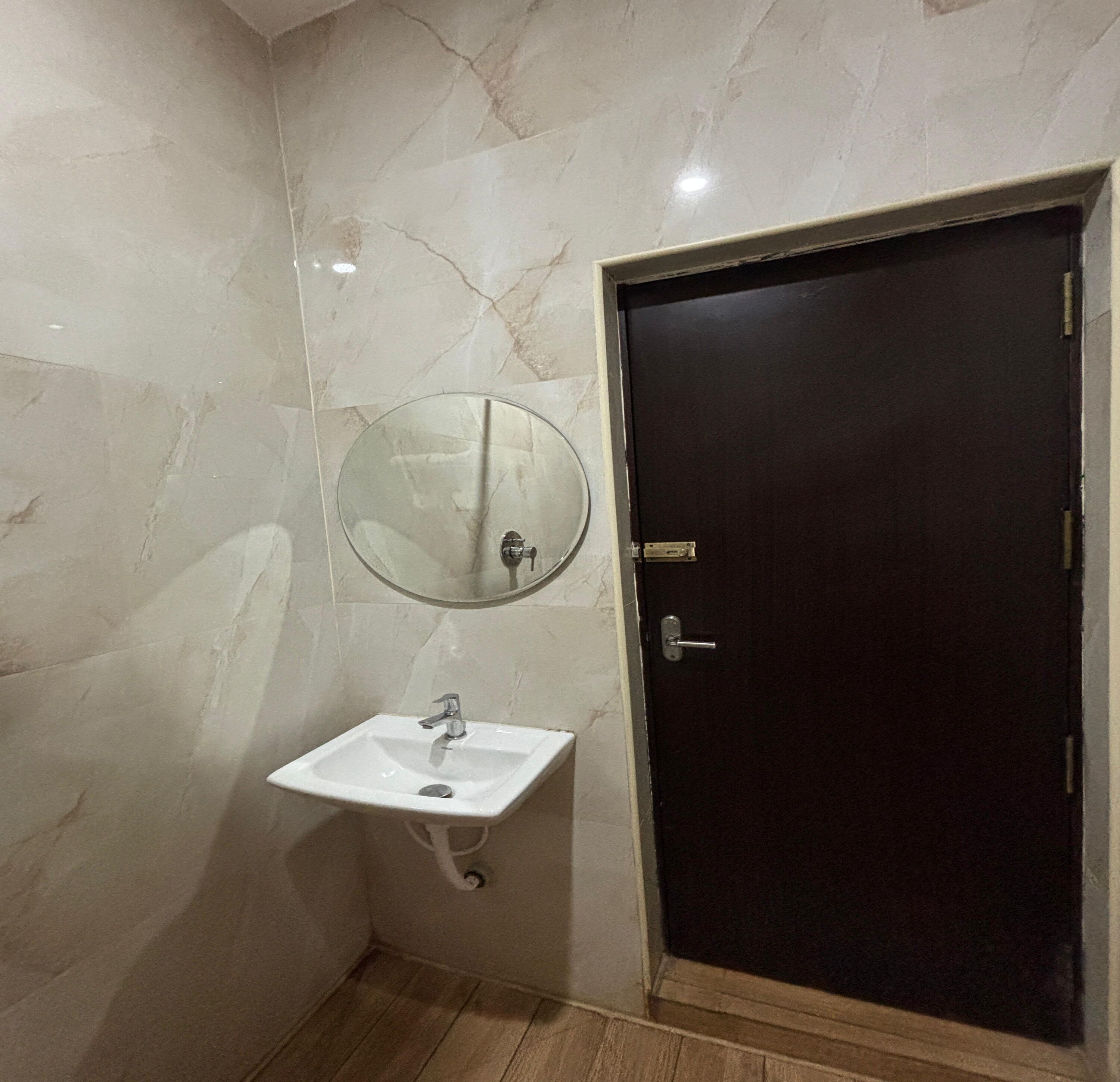 A bathroom with a white sink, a round mirror, and a dark door.