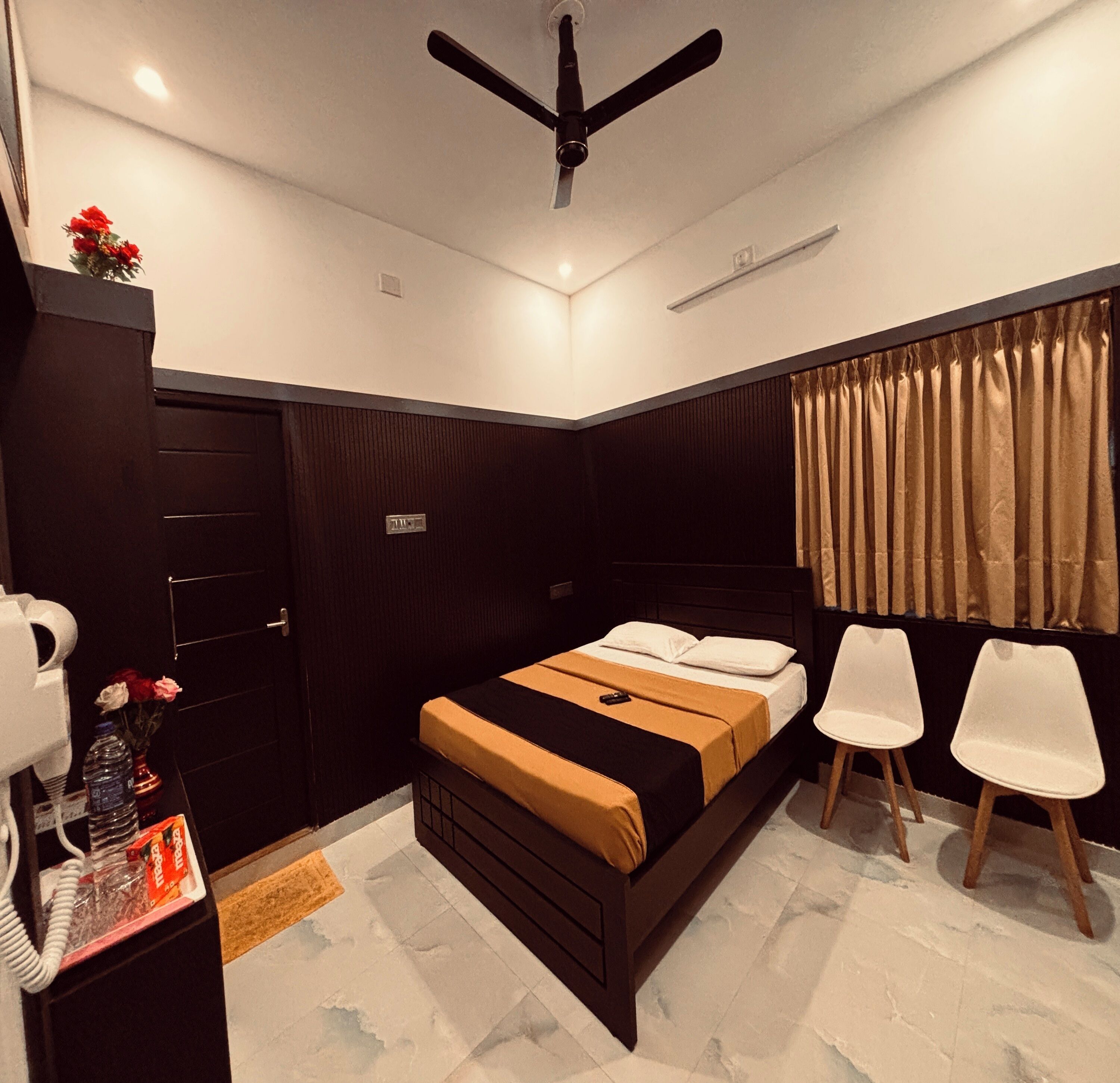 A bedroom with a bed, two chairs, a desk with a telephone, and a ceiling fan.