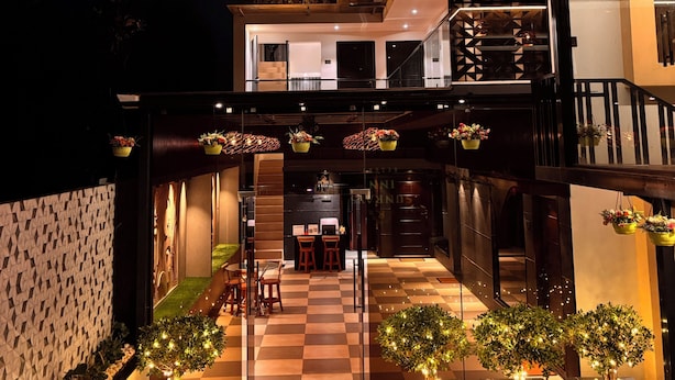 A hotel with a checkered outdoor seating area, a balcony with hanging plants, and a neon sign. - Sun Rays Inn (Yercaud)