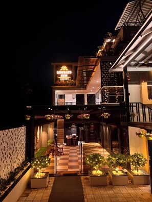 A hotel with a checkered outdoor seating area, a balcony with hanging plants, and a neon sign. - Sun Rays Inn (Yercaud)