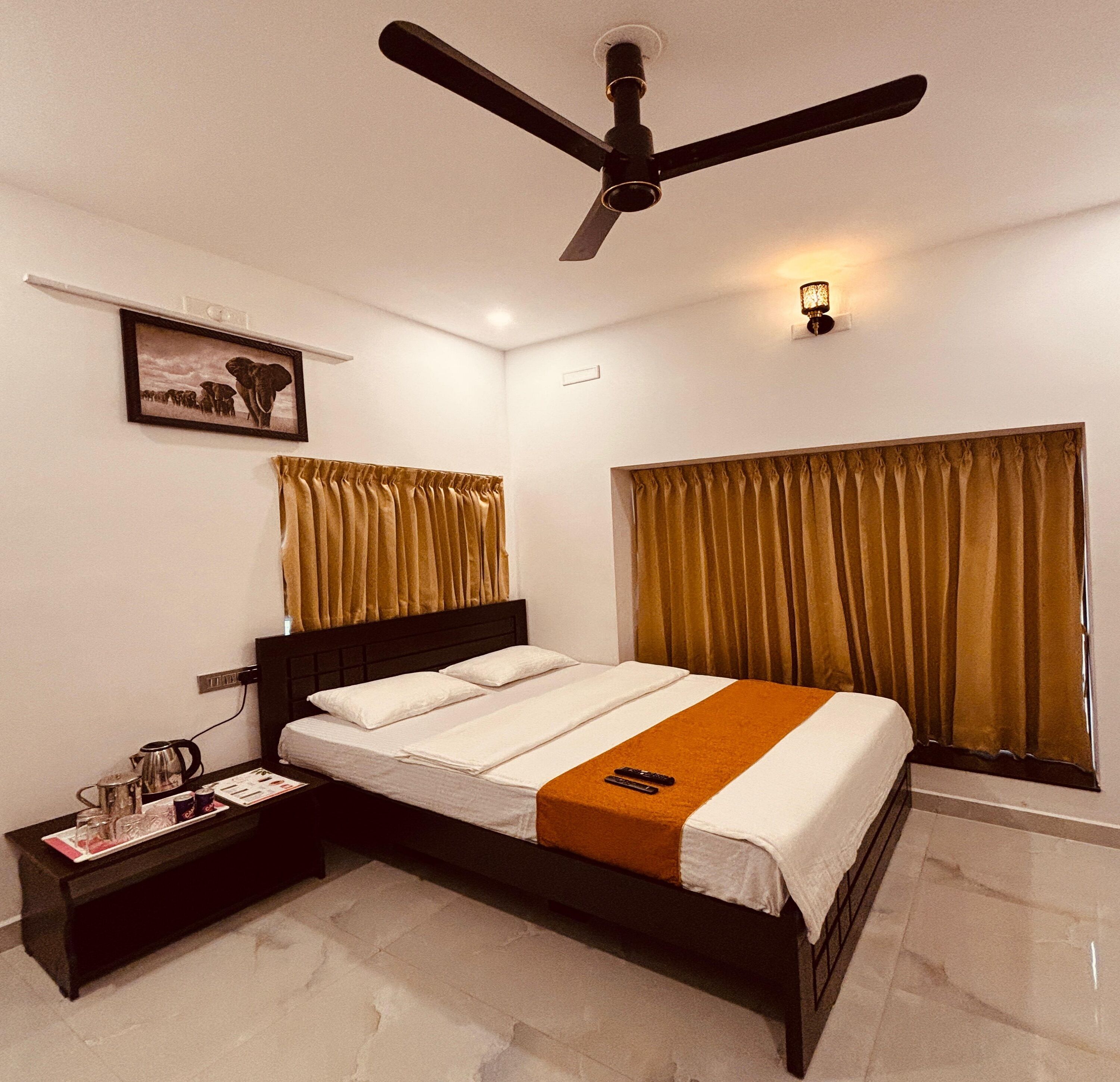 A hotel room with a bed, a nightstand, a ceiling fan, a wall-mounted light, and a window with curtains.