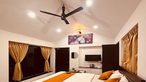 A modern bedroom with a large bed, a ceiling fan, a flat-screen TV, and a painting above the bed. - Sun Rays Inn (Yercaud)