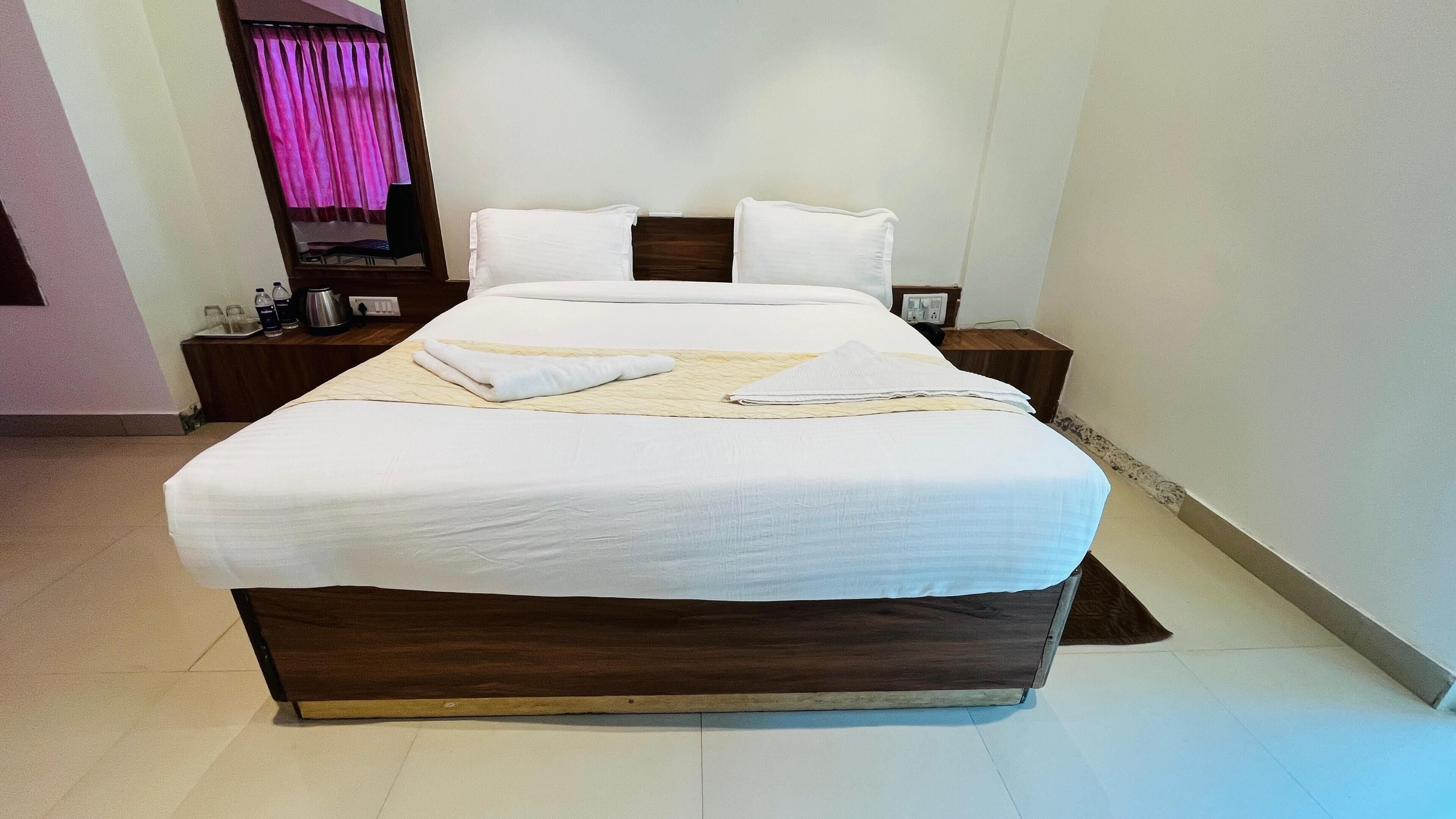A neatly made bed with white linens, a wooden headboard, and a bedside table with a lamp and a small clock.