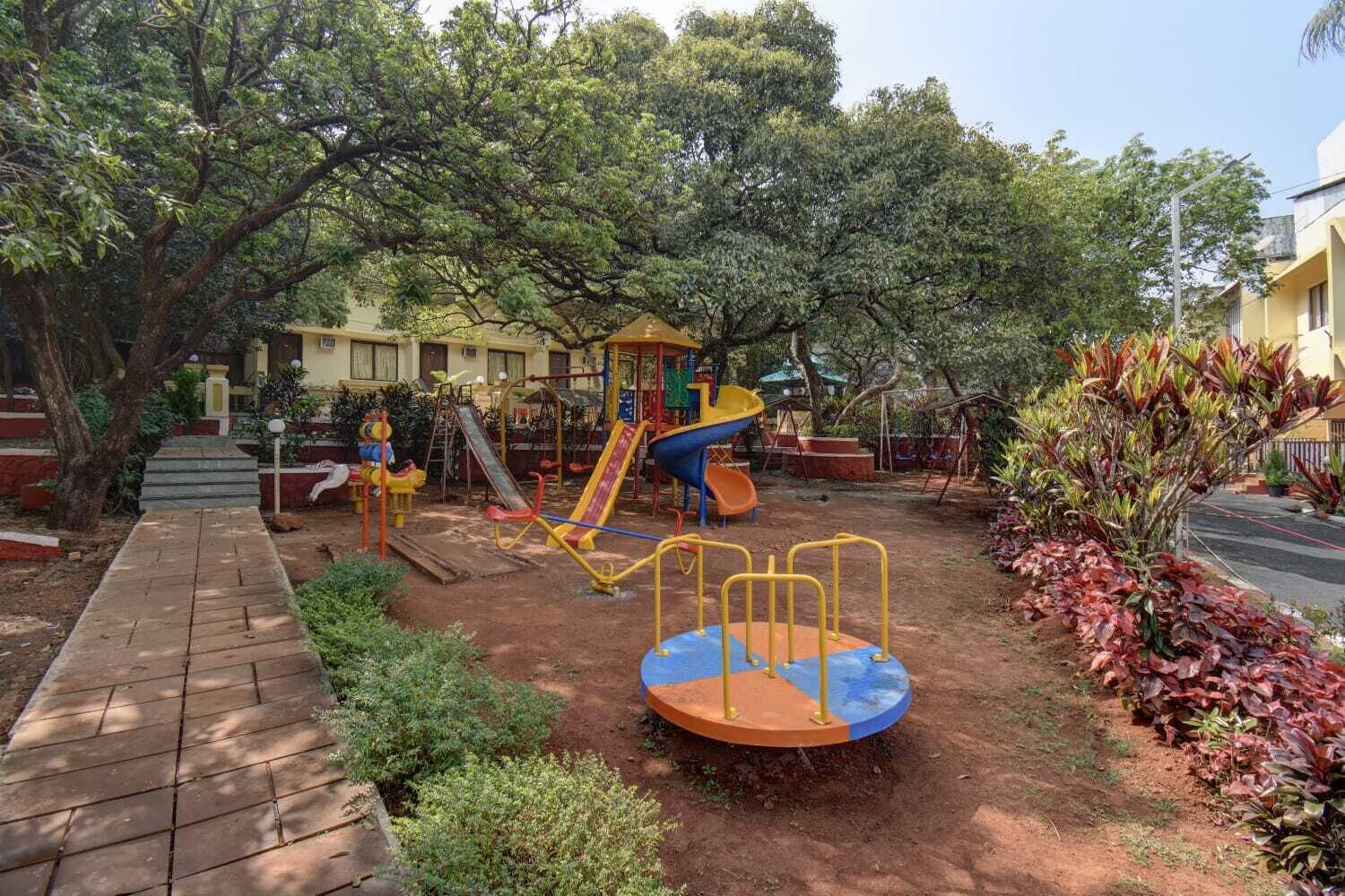 A playground with various play structures, a paved walkway, and surrounding greenery.