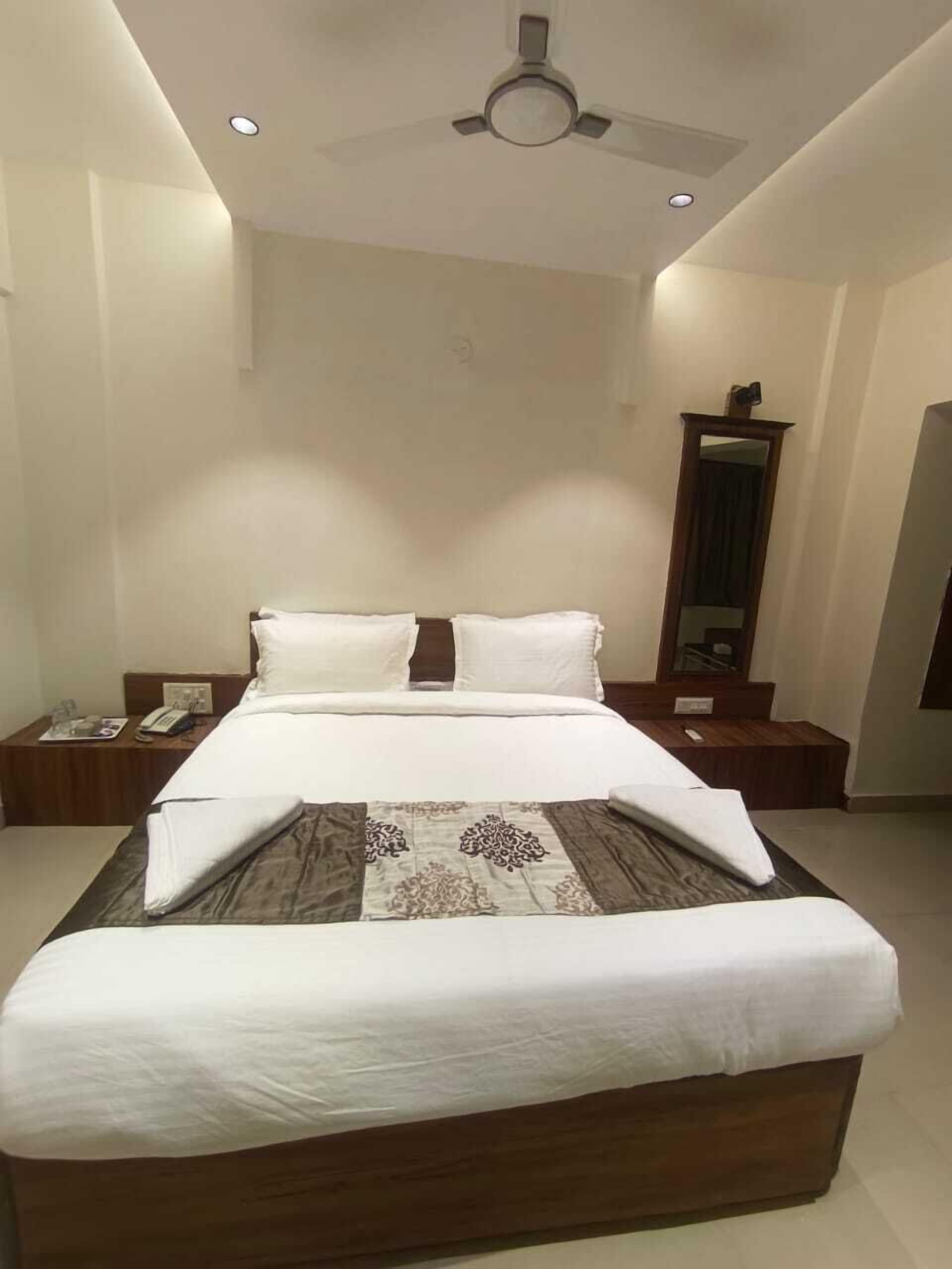 A modern bedroom with a large bed, a ceiling fan, and a nightstand with a phone and a magazine.