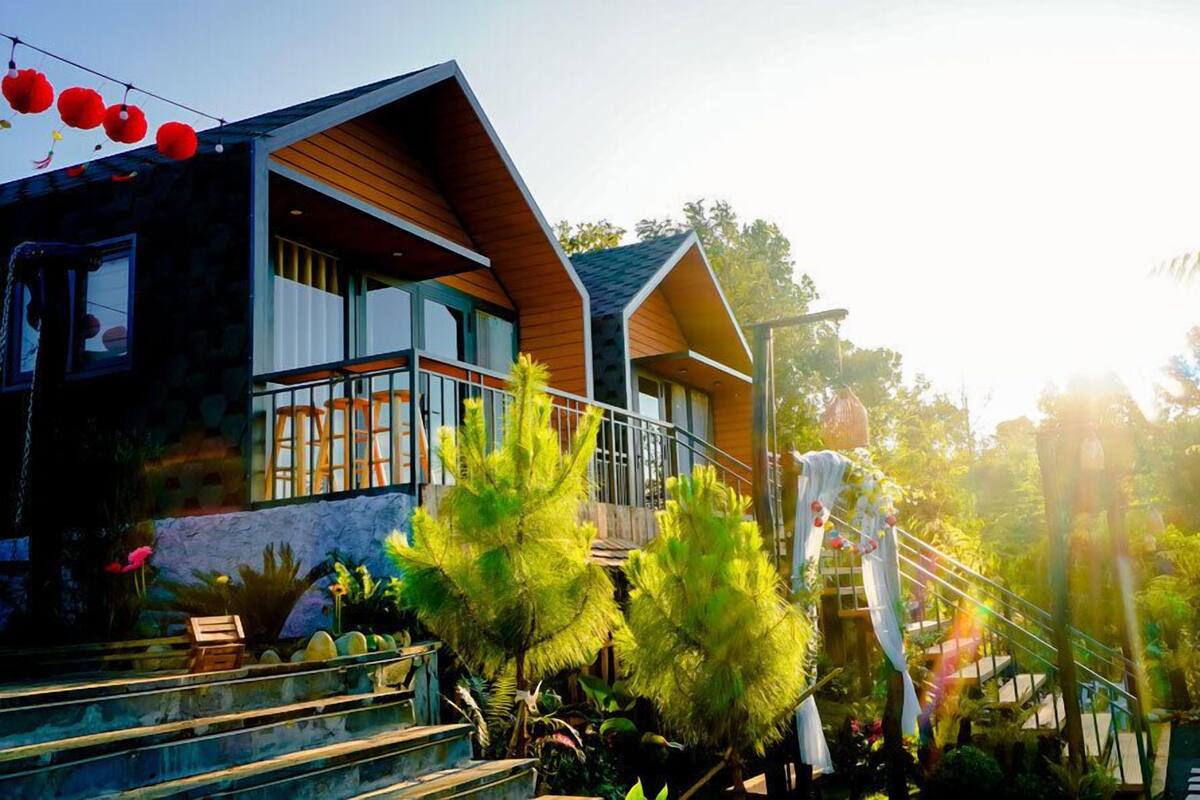 A modern house with a wooden facade, a balcony, and a staircase leading to a deck surrounded by tropical plants.