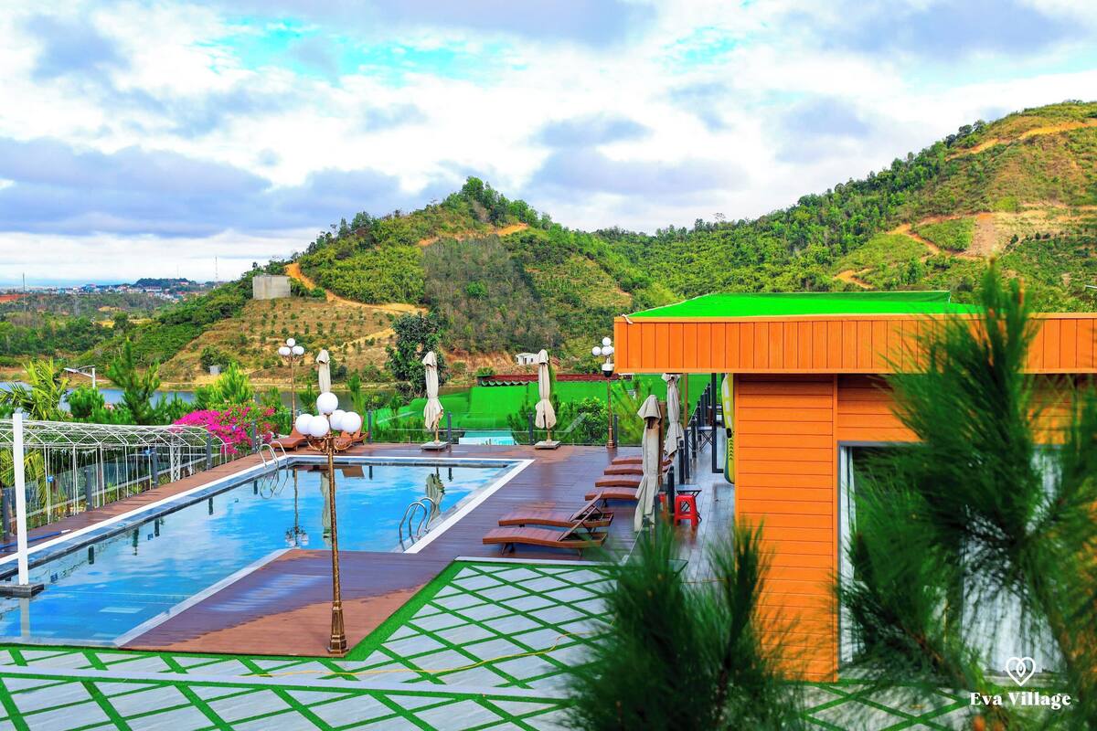 A swimming pool with a green deck, lounge chairs, and umbrellas, surrounded by lush greenery and hills.