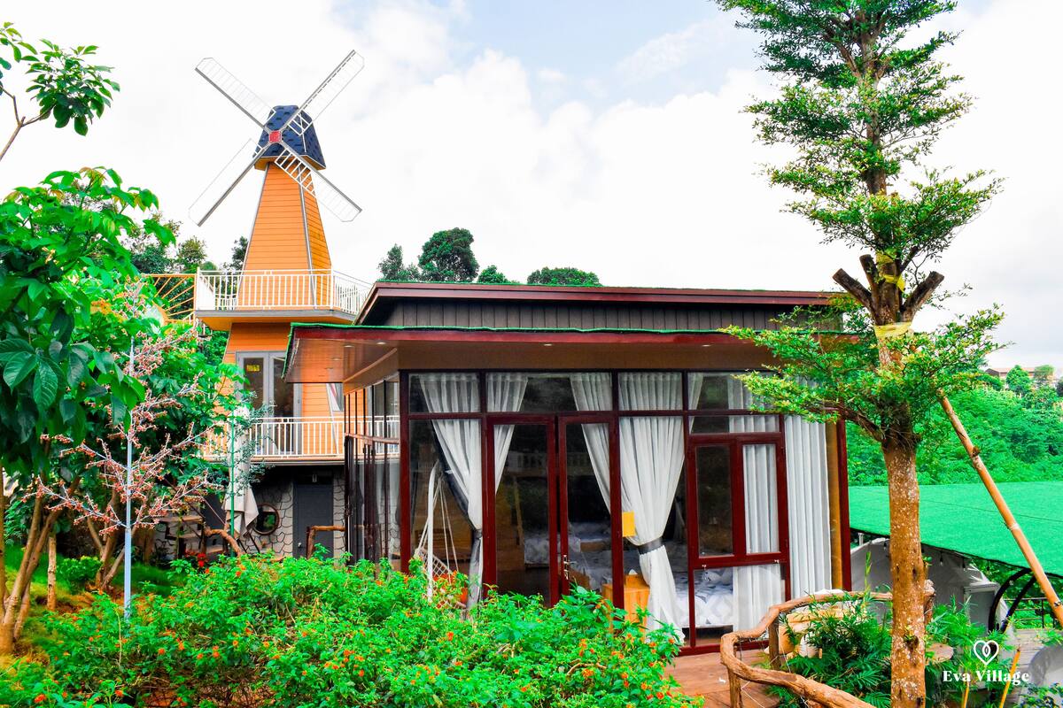 A traditional windmill, a wooden house with a balcony, and lush greenery.