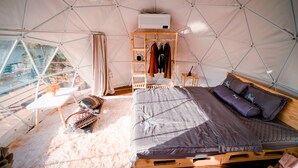 A tented accommodation with a bed, a small table, and a clothing rack. - EVA VILLAGE (Dong Gia Nghia)