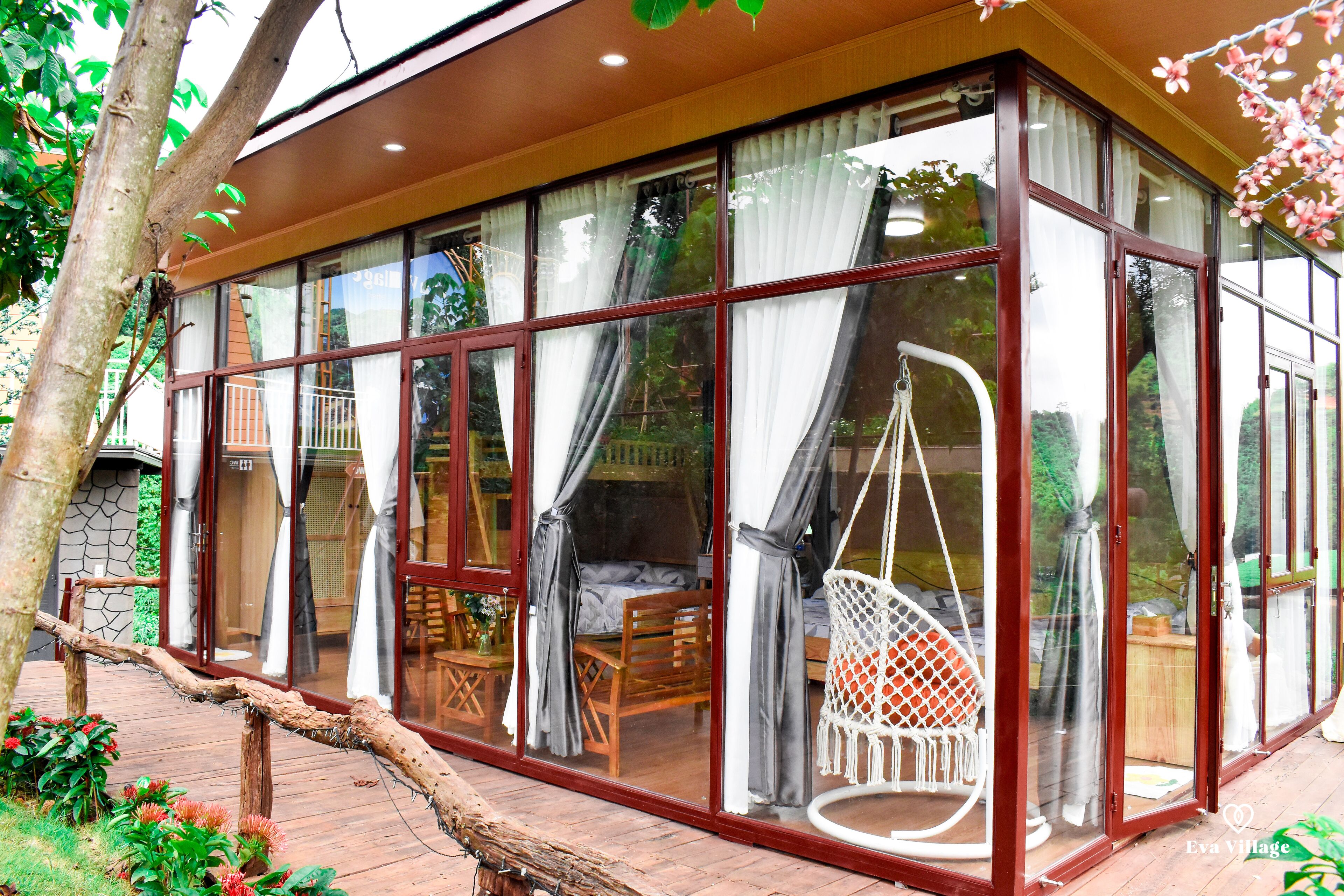 A glass-enclosed room with a wooden floor, a hanging chair, and a bed with curtains.