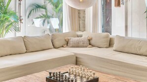 Una sala de estar moderna con un amplio sofá modular, una mesa de centro de madera con un tablero de ajedrez y un gran ventanal con cortinas.