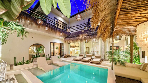 Una piscina interior con zonas de descanso, ventiladores de techo y plantas tropicales.