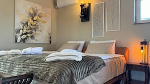 Cama bem arrumada com manta cinza e toalhas brancas, mesa de cabeceira de madeira com abajur e obras de arte nas paredes.