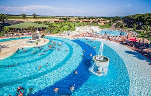 Una gran piscina al aire libre con múltiples carriles, un tobogán acuático y una zona circundante con tumbonas y sombrillas.