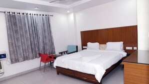 A hotel room with a large bed, a wooden headboard, a desk, a chair, and a window with curtains. - Hotel Pardesi Cardo (Saharsa)