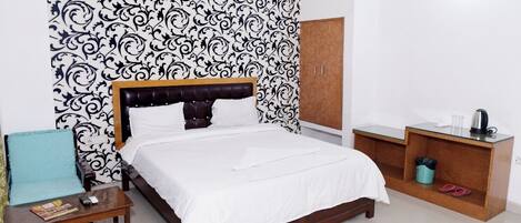 A neatly arranged bedroom with a bed, a wooden nightstand, a wardrobe, and a small table with a kettle and cups.