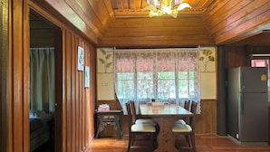A wooden-paneled room with a dining table, chairs, a chandelier, and a refrigerator. - Blooming Village by Aforetime (Koh Samui)